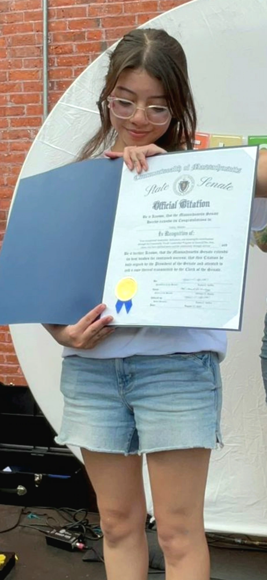 A young GEMS volunteer reading her State Senate citation with a proud smile