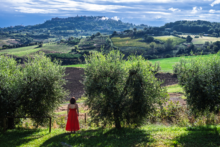 A woman in a red dress before the olive groves and a Tuscan hilltop town