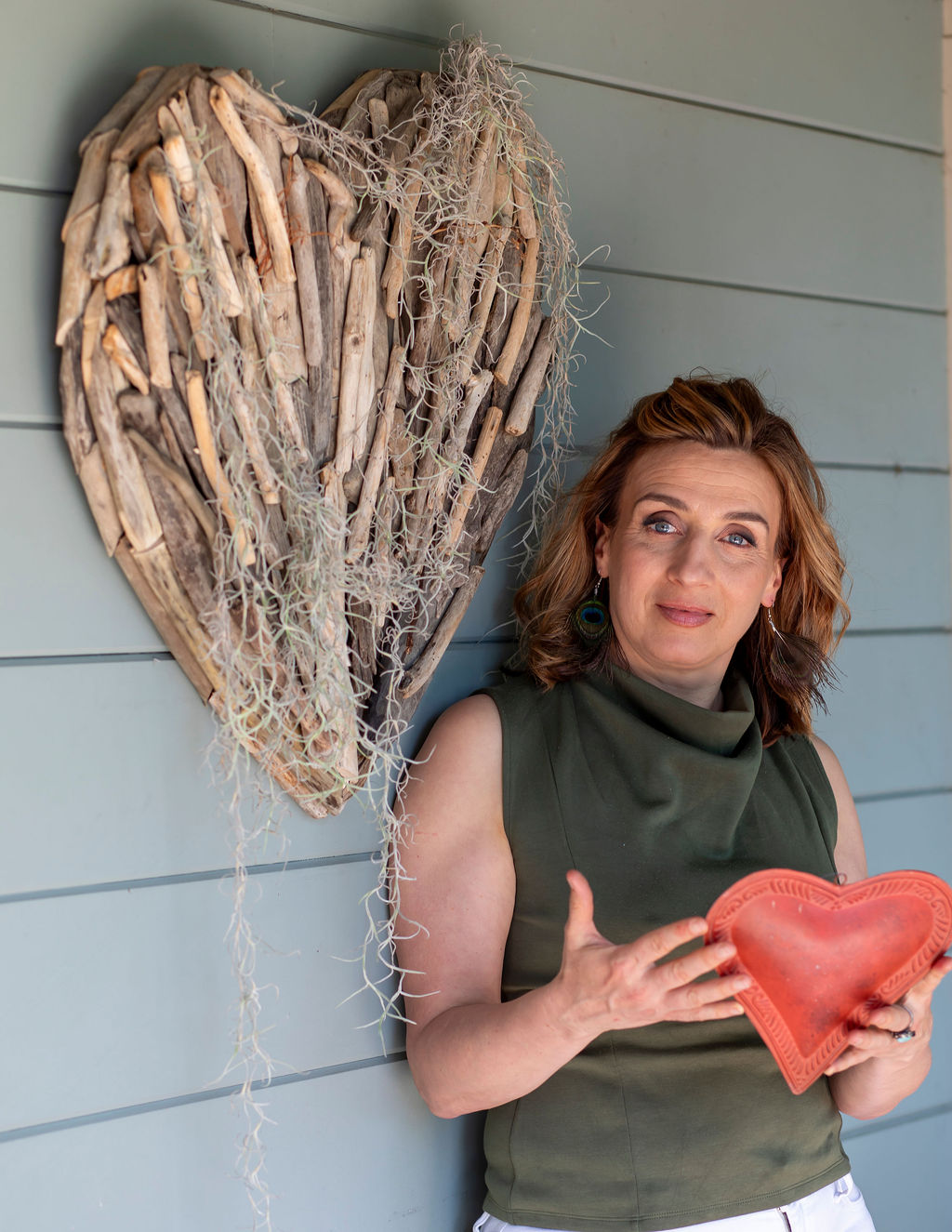 Monica holding a ceramic heart beside a driftwood heart