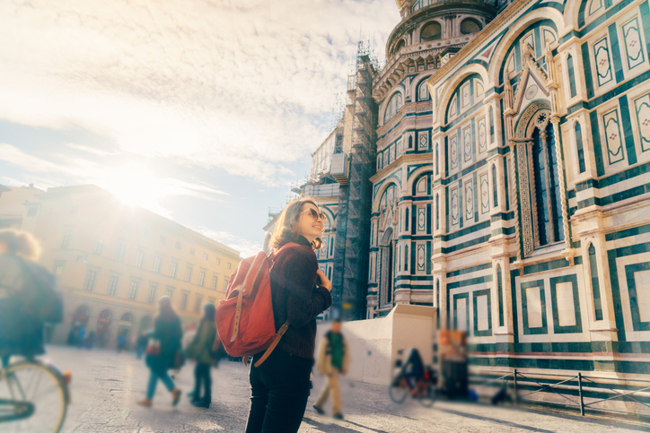 A woman with a red backpack in golden light before the Florence cathedral